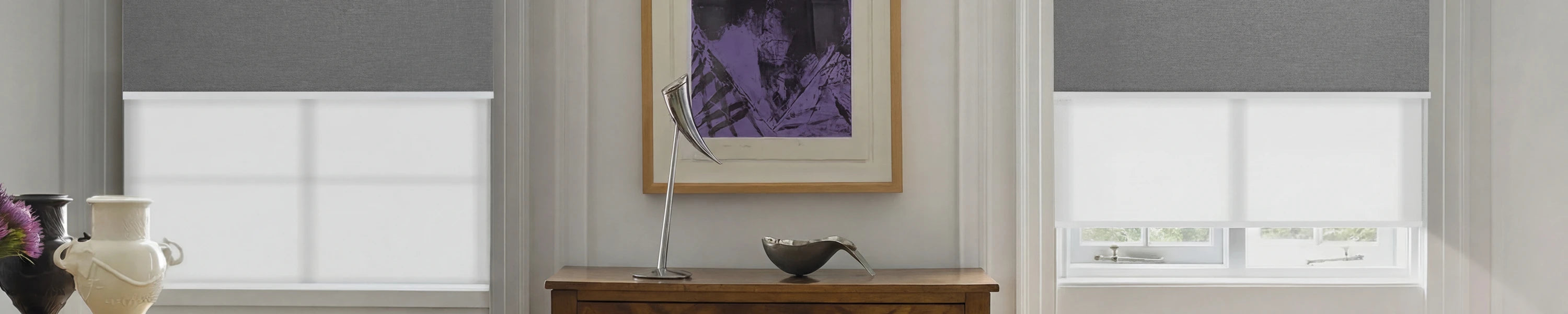 White roller blinds in a room with a painting and dual roller shades.