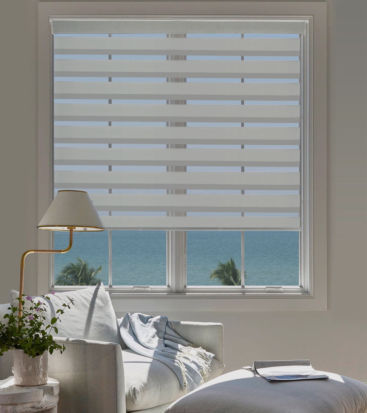 Living room with a large window featuring striped window blinds, a lamp, and a couch.