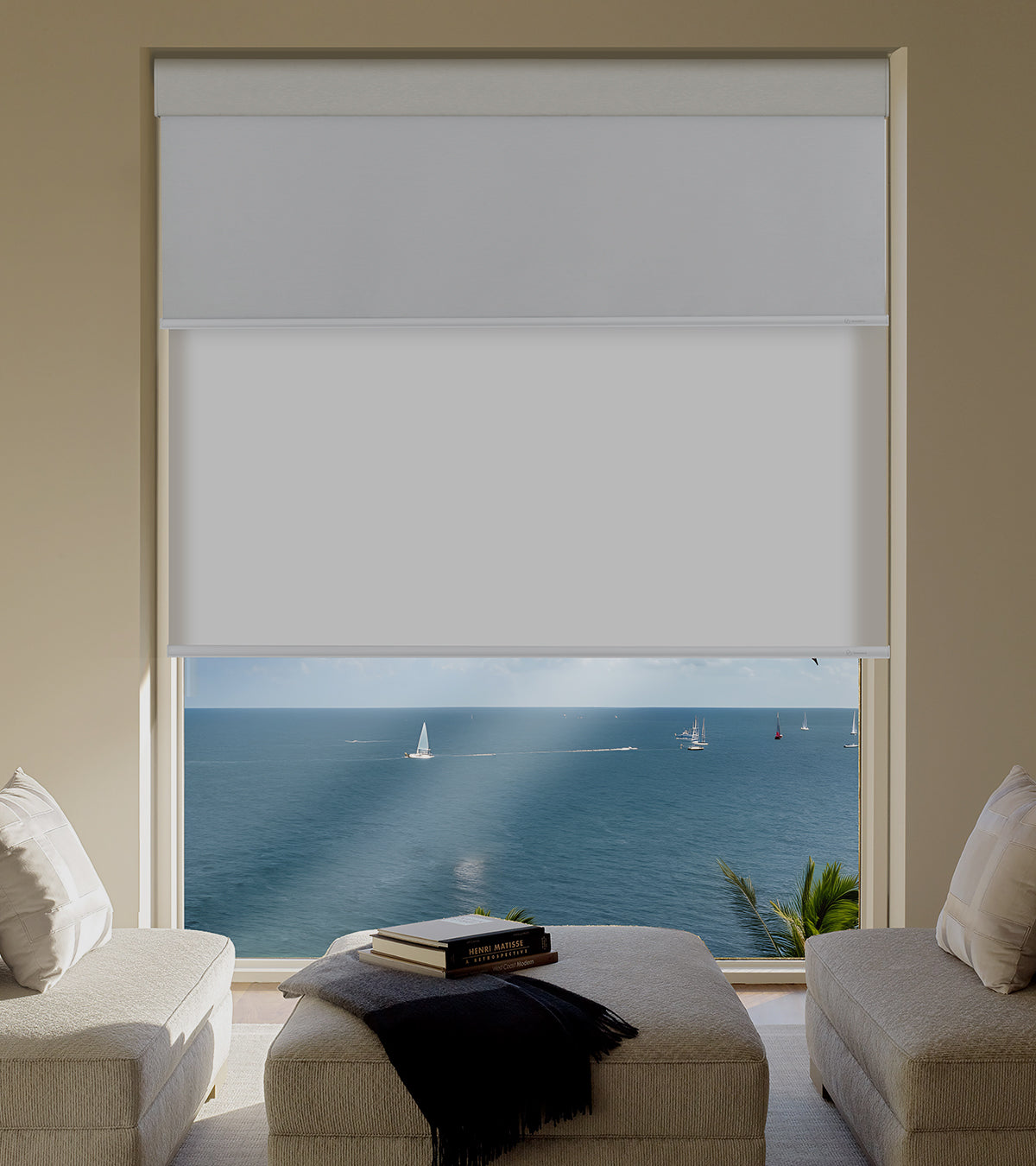 Living room with a large window featuring a roller blind, showing a view of the ocean with sailboats.