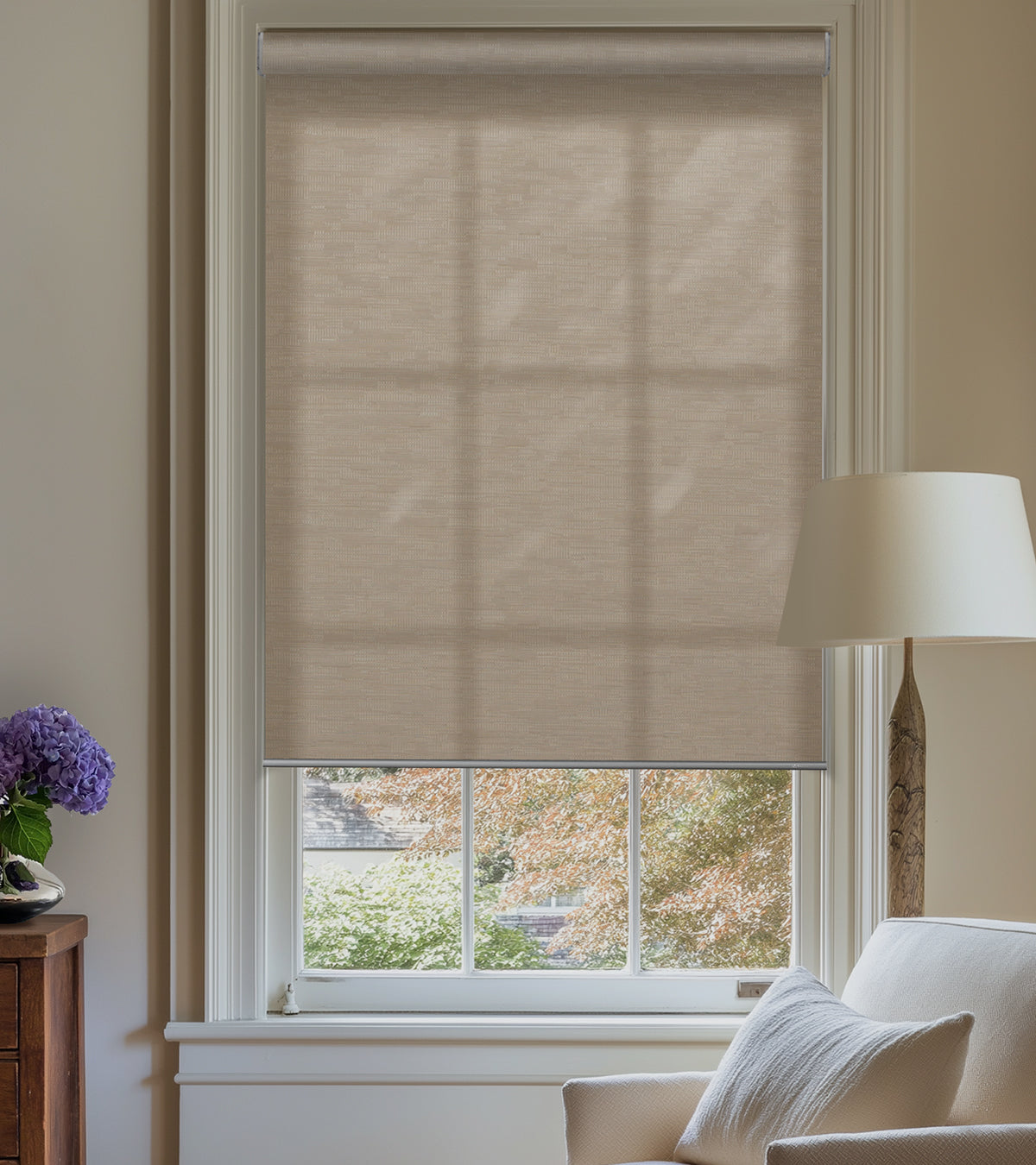 Beige roller blind on a window with a lamp and decorative elements in the room.