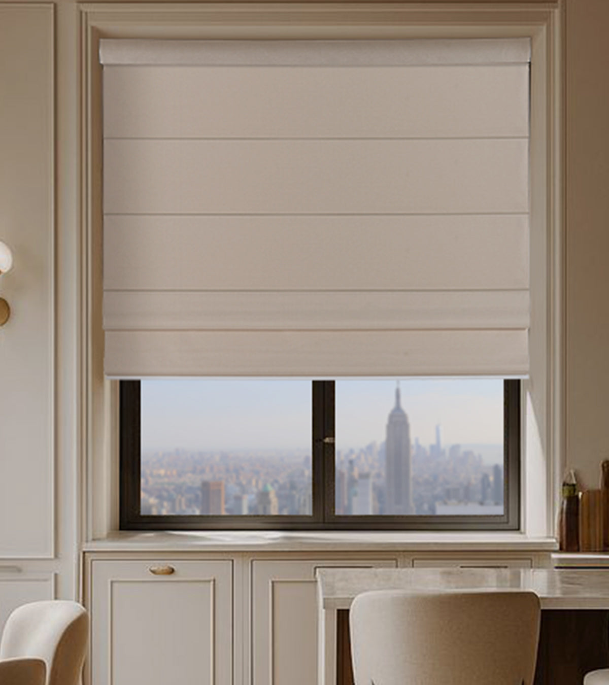Beige roman blinds covering a window with a cityscape view, in a room with light-colored walls and furniture.