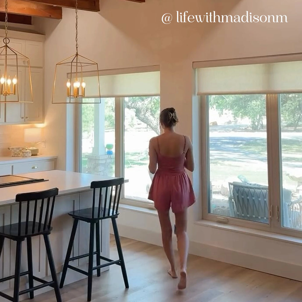 Woman in a pink dress standing by a window in a modern kitchen with roller shades.