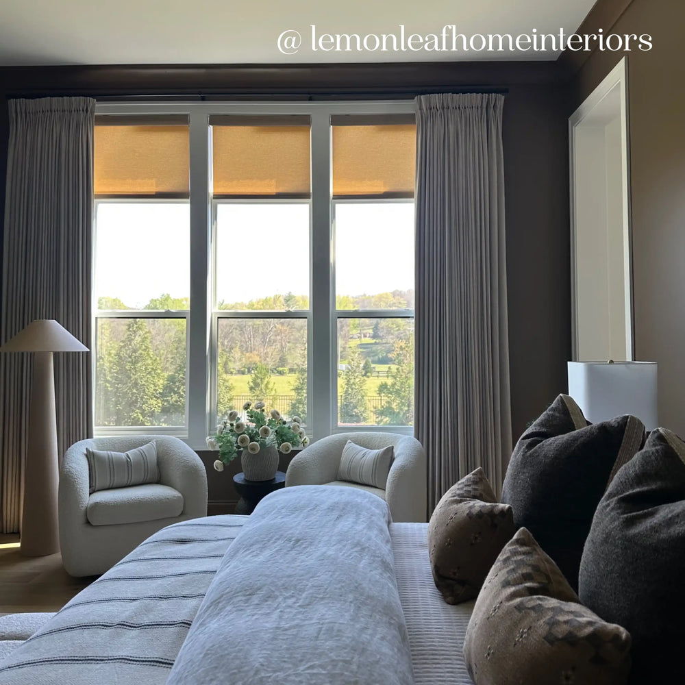 Modern bedroom with large windows, gray curtains, and a cozy bed with pillows.