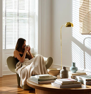A woman sits in a cozy living room with Venetian Blinds.