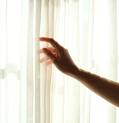 Hand touching a sheer white curtain.