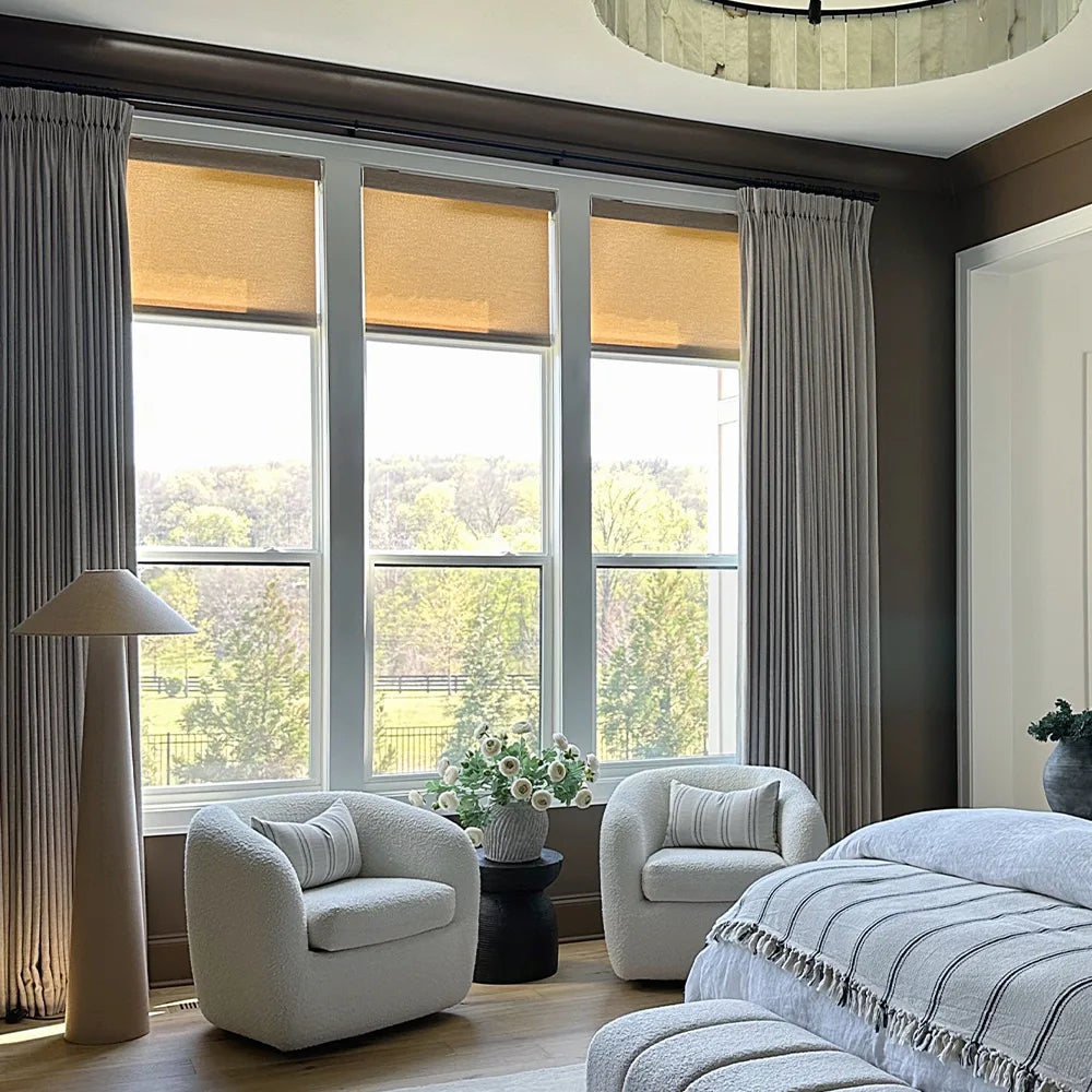 Modern living room with roller shades and curtains, gray chairs, and a lamp.