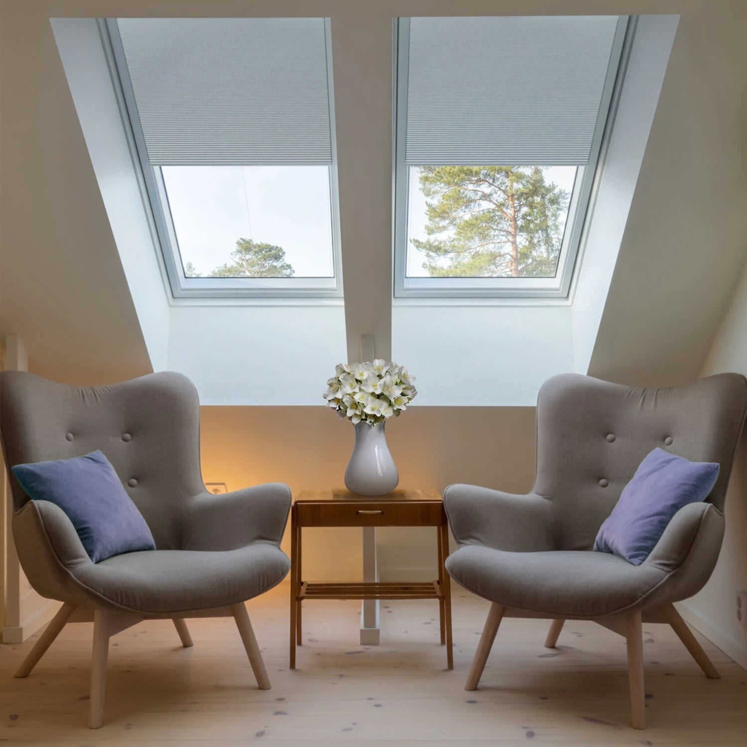 Two gray armchairs with blue cushions in a room with skylights and a small table with flowers.