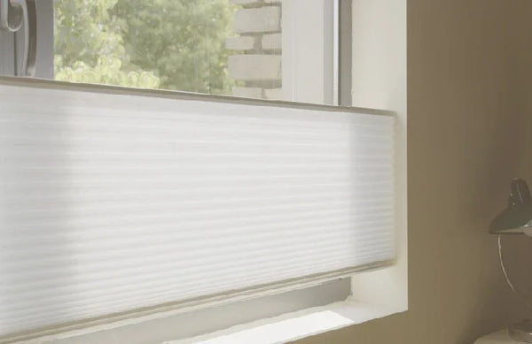 Window with white blinds partially open, showing a stone wall and greenery outside.