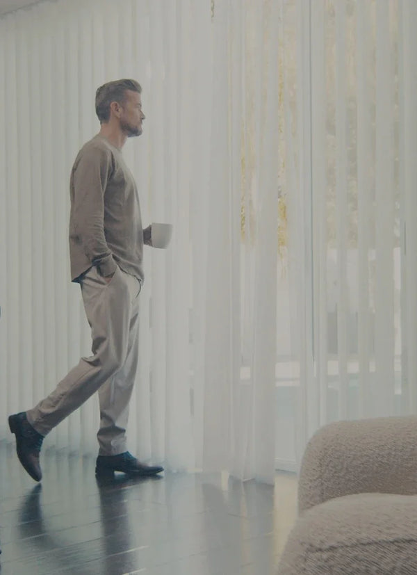 Man walking in a room with sheer curtains and a chair.
