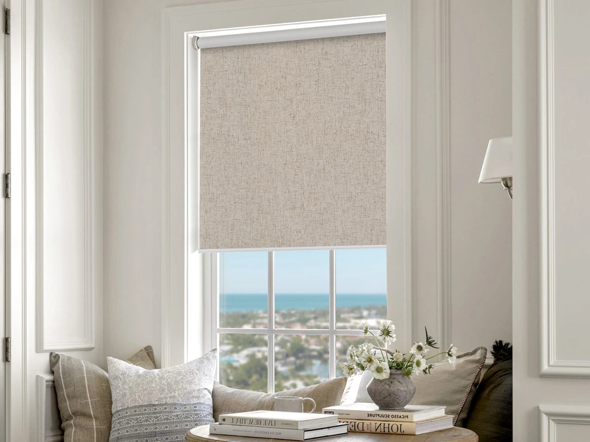 Window with no drill roller blind, view of ocean and cityscape, interior decor with books and flowers.