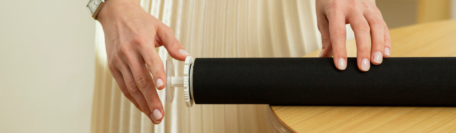 A person holds no drill roller shades on a table background.