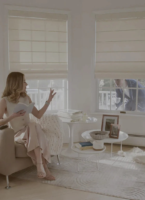 Woman sitting in a modern living room with white blinds and decor.