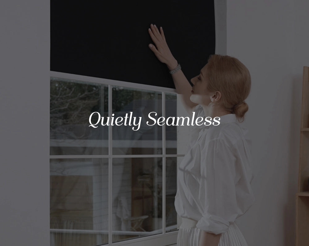 Woman in a white outfit adjusting blackout shades in a room with a window.