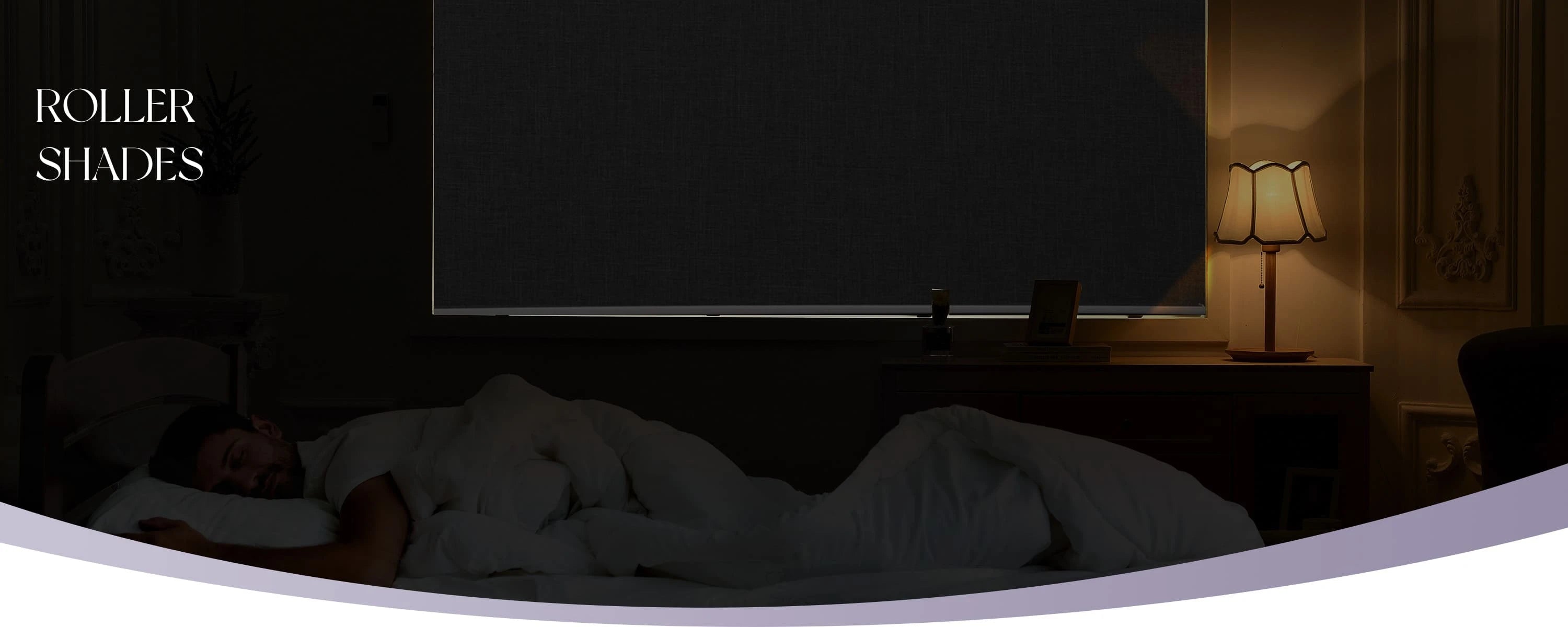 Person sleeping in a dark bedroom with roller shades partially covering a window.