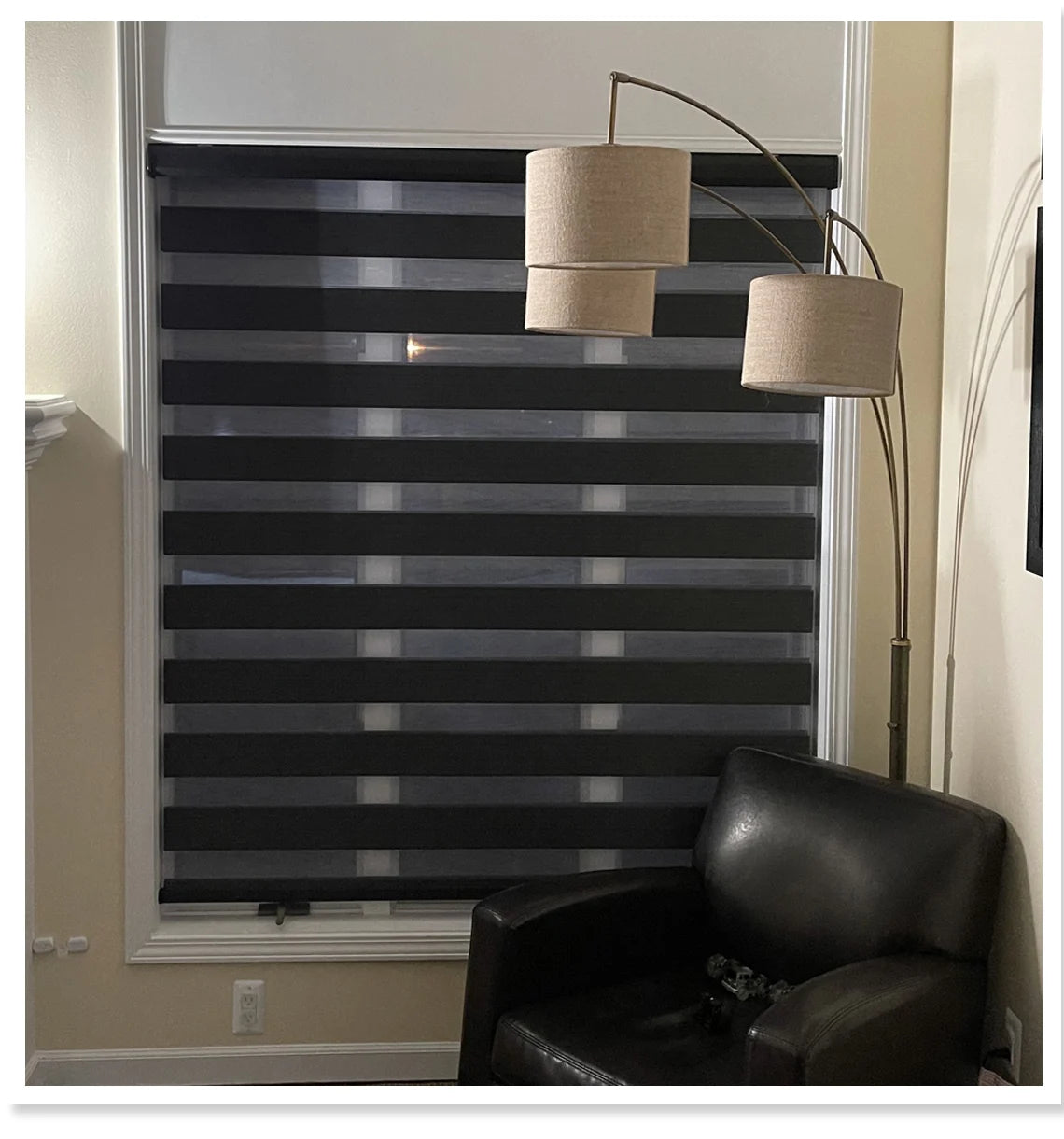 Window with black zebra blinds, a black chair, and a floor lamp in a room.