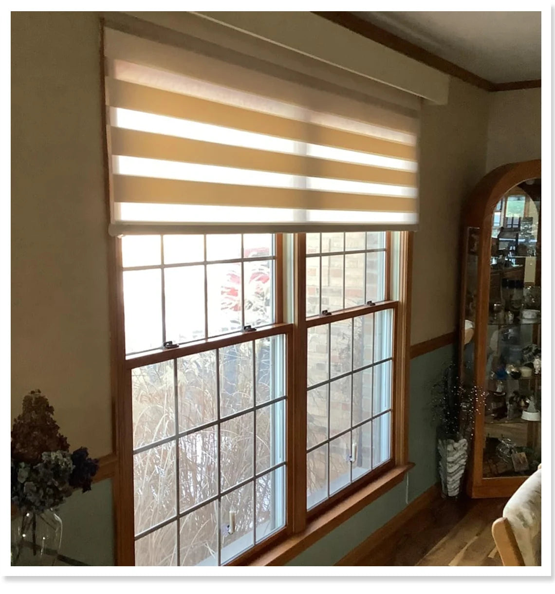 Window with zebra blinds in a room with a bookshelf and decor items.
