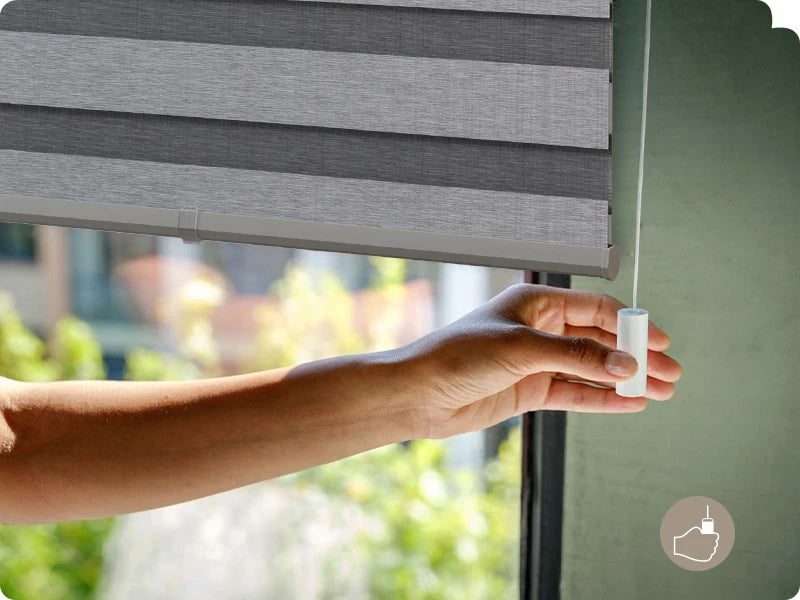 Person adjusting a gray horizontal zebra blinds with a blurred green outdoor background